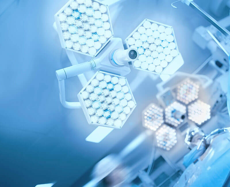 Imagem de um bloco operatório sofisticado e moderno, em tons de azul e com duas luzes cirúrgicas de leds apontadas para a câmara