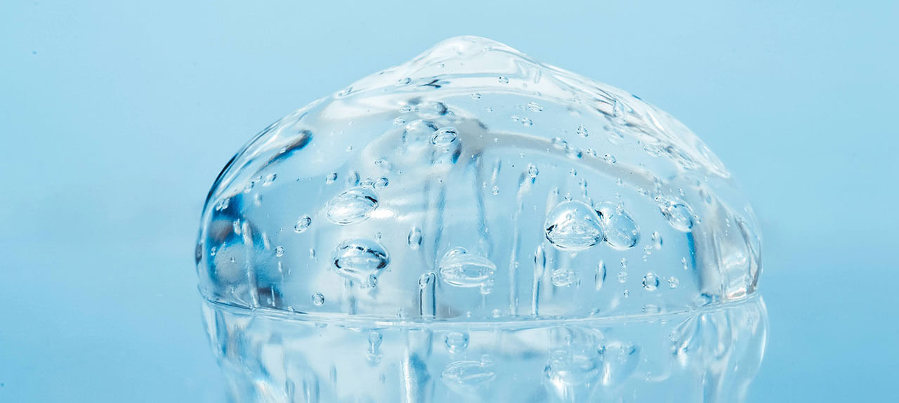 Imagem ampliada de uma gotícula de gel de ácido hialurónico, sob um fundo azulado