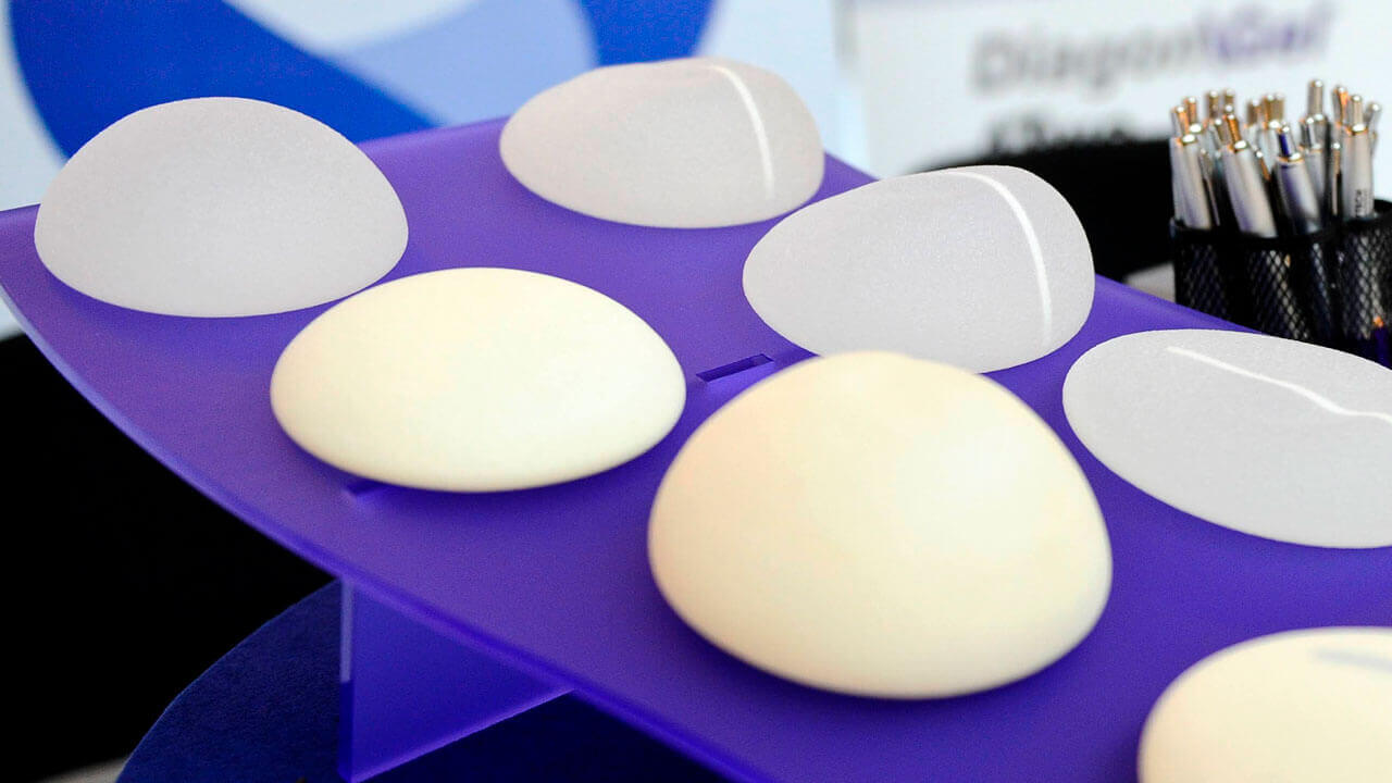 imagem demonstrando vários implantes mamários de silicone, com diversas formas e tamanhos, sob uma plataforma azul