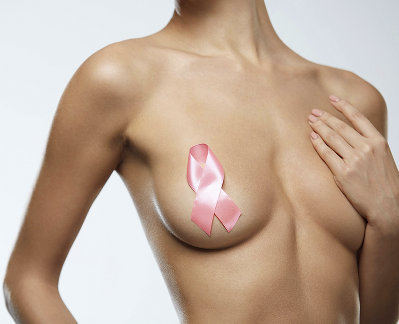 imagem frontal do tronco de uma mulher despida sob um fundo branco, com o mamilo direito coberto por um laço cor-de-rosa da Liga Contra o Cancro e o mamilo esquerdo tapado pela mão